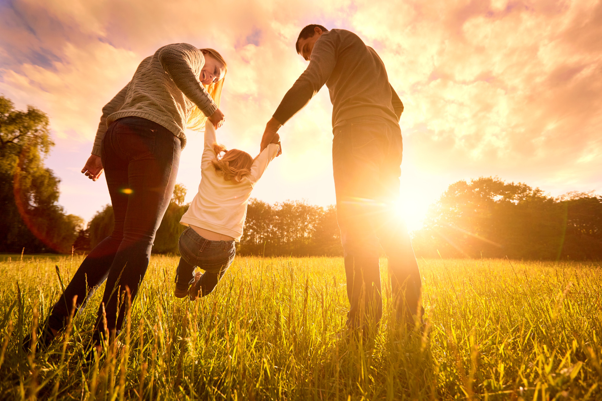Parents hold baby's hands. Happy family in park evening Happy family in the park evening light. The lights of a sun. Mom, dad and baby happy walk at sunset. The concept of a happy family.Parents hold the baby's hands.